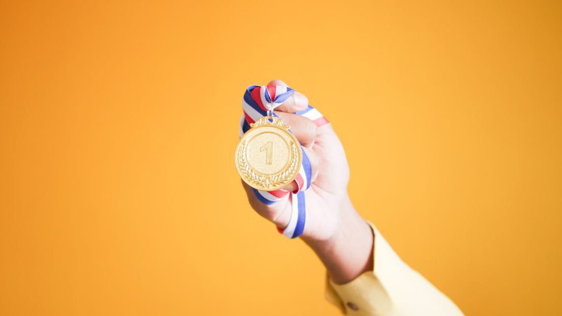 A person holding a medal in orange background