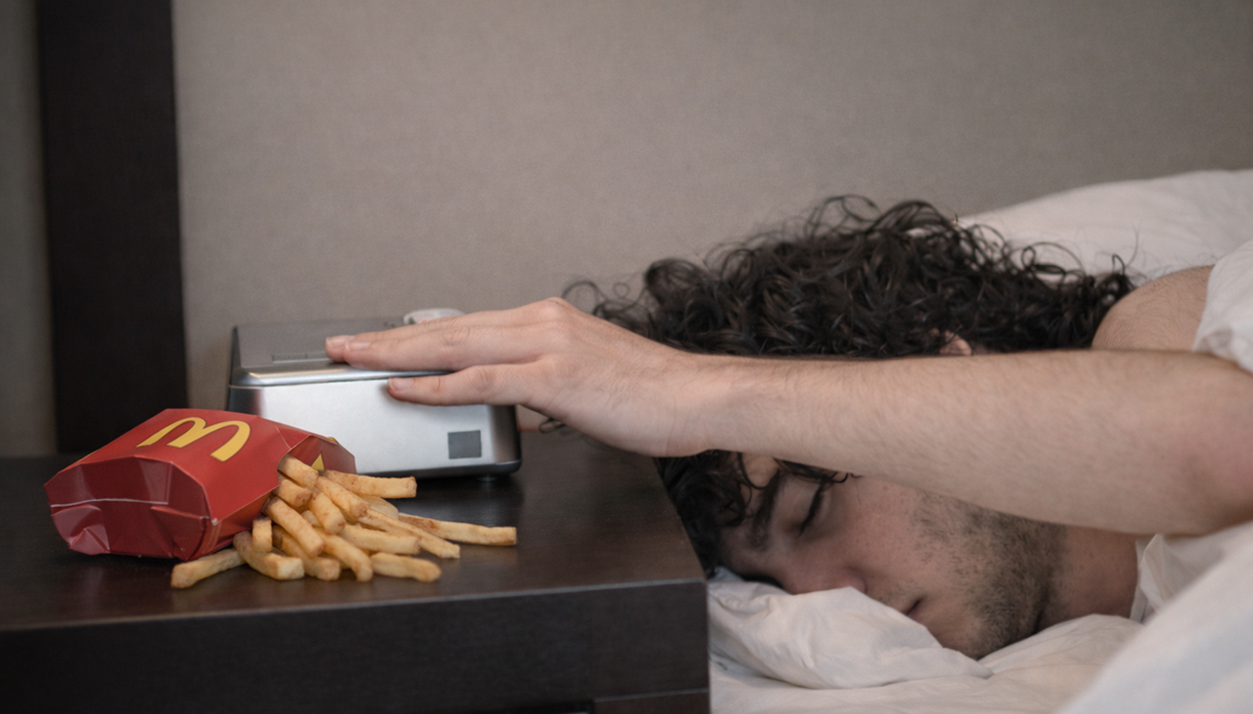 An image from the video wherein a sleeping man was awaken by his alarm and turned it off, emphasising the McDonald's fries on the table as well